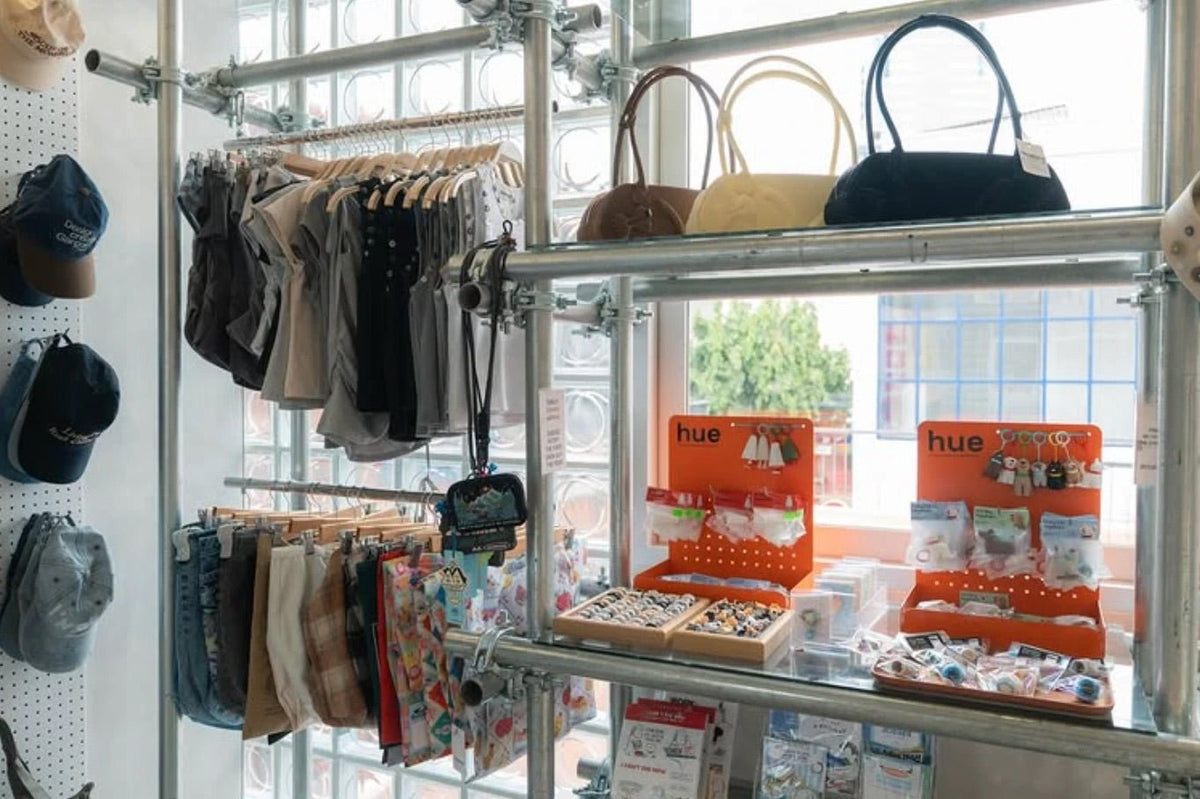 Scaffold-pipe shelving by a glass-block window with bags, clothing and accessories