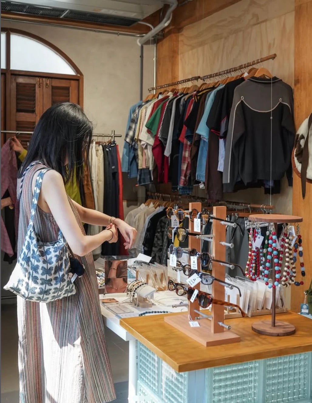 A shopper browsing sunglasses and jewelry with clothing racks behind
